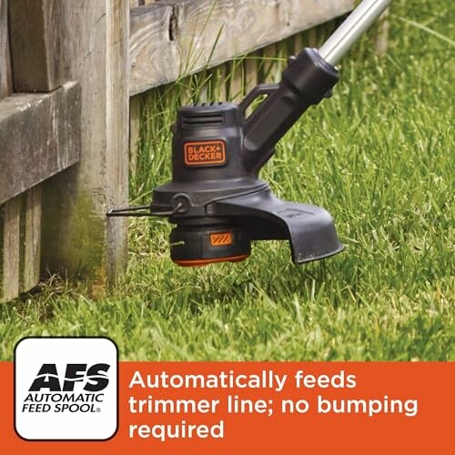 Black and Decker trimmer cutting grass near a wooden fence with automatic feed spool feature.
